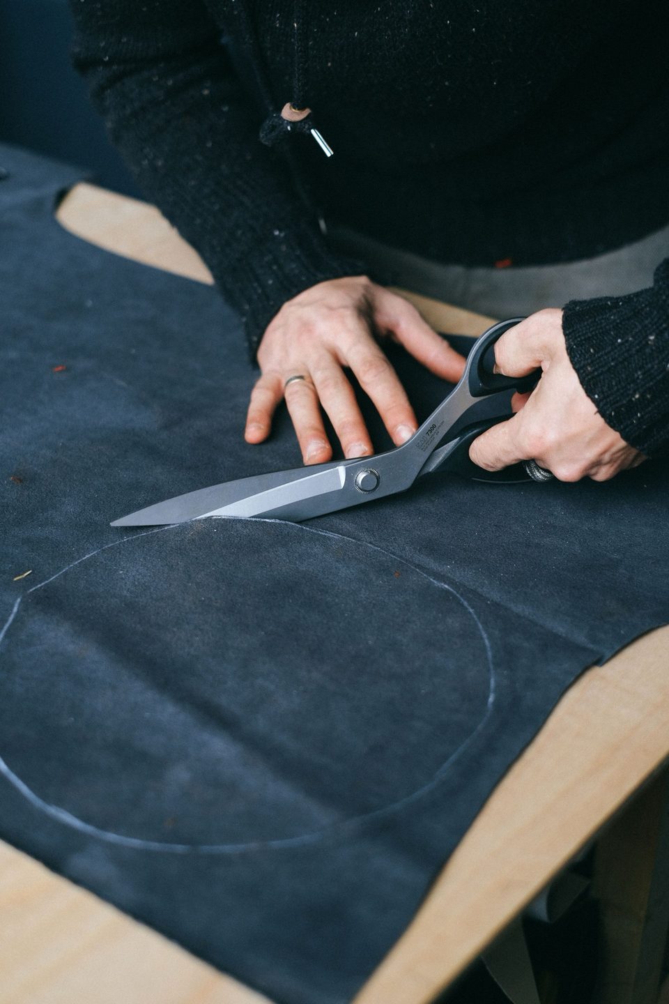 A tailor cutting dark cloth with shears on a workbench